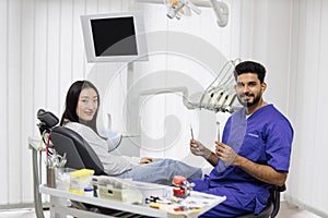 Asian woman sitting in the dentist& x27;s chair in light modern dental clinic with attractive man dentist