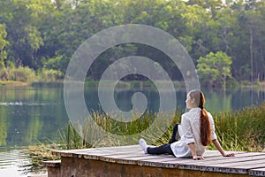 Asian woman sitting on the edge of dock with peaceful natural park during summer looking at turquoise lake for serene and