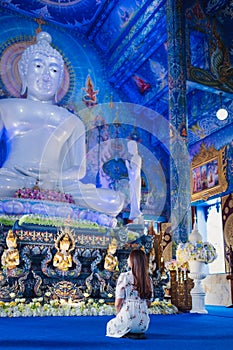 A woman sitting in front of buddha statue at Wat Rong Suea Ten, The blue temple in Chiang Rai, Thailand