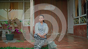 Asian woman sitting in the front house enjoying the village in the morning while wearing a grey dress and black skirt