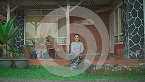 Asian woman sitting in the front house enjoying the village in the morning while wearing a grey dress and black skirt