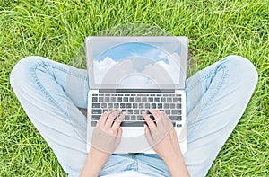 Asian woman sitting on grass floor in the garden textured background for use a notebook computer with blue sky in screen of
