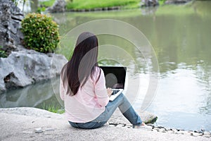 Asian woman sitting green park using laptop computer. Woman working on laptop happy entrepreneur business using notebook with