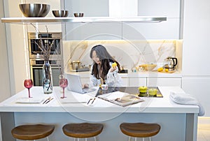 asian woman is sitting in kitchen workplace desk and working on laptop. Online Recipe site.