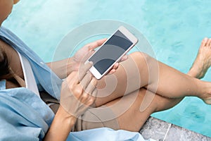 Asian woman sitting near swimming pool using mobile phone. Young traveler girl working on cell phone during her summer holiday.