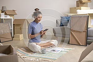 Asian woman sitting in new house using smartphone buying decorations online after moving in