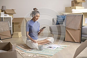 Asian woman sitting in new house using smartphone buying decorations online after moving in