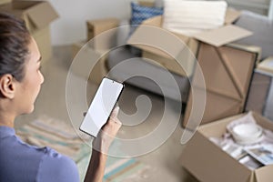 Asian woman sitting in new house using smartphone buying decorations online after moving in