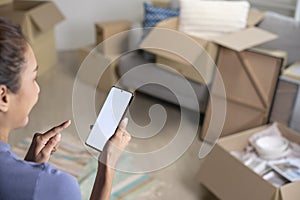 Asian woman sitting in new house using smartphone buying decorations online after moving in