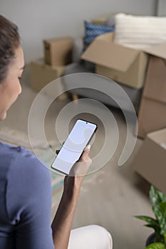 Asian woman sitting in new house using smartphone buying decorations online after moving in