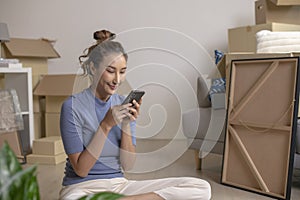 Asian woman sitting in new house using smartphone after moving in