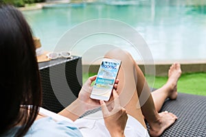 Asian woman sitting by the pool while using mobile phone. Female using travel application for flight tickets and hotel room online