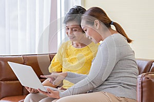 Asian woman sitting in on sofa with her daughter and video call talk to someone in notebook laptop computer with happy