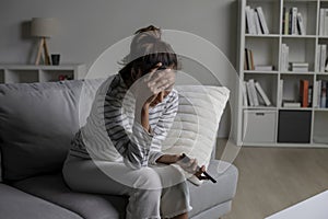 Asian woman sitting on sofa holding phone feeling disappointed, sad, upset.