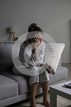 Asian woman sitting on sofa holding phone feeling disappointed, sad, upset.