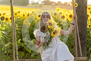 asian woman sitting on swing in a white dress with a bouquet and take selfie in the field of sunflowers in Yorkshire