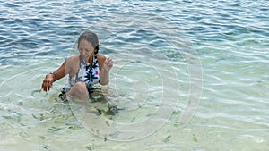 Asian woman sitting in water surrounded by tropical fish