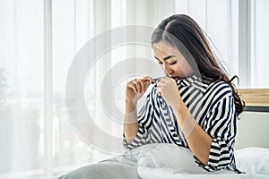 Asian woman sitting on a white bed, she open her shirt and bent down to see her breast size, concept for women who are concerned