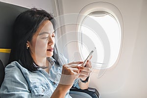 Asian Woman sitting at window seat in airplane and turn on airplane mode on mobile phone before take off