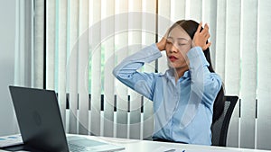 Asian woman sitting at work caused a headache so she gently rubbed her head with her hand