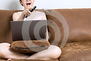 Asian woman sitting and working on the sofa, feeling sleepy, using the remote control to turn off the TV. Work from home concept