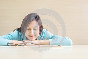 Asian woman sleep by lied on desk with happy face in rest time from reading book on blurred wooden desk and wall textured backgrou