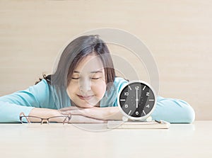 Asian woman sleep by lied on desk with happy face in rest time from reading book with clock show the time in 6 o`clock on desk