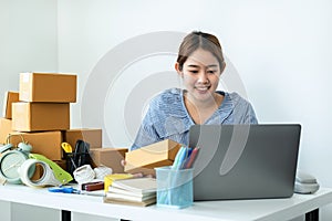 Asian woman small business owner holding box of parcel in hands and checking order on laptop while courier working