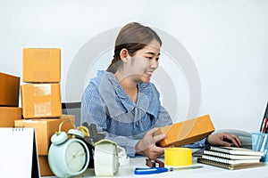 Asian woman small business owner holding box of parcel in hands and checking order on laptop while courier working