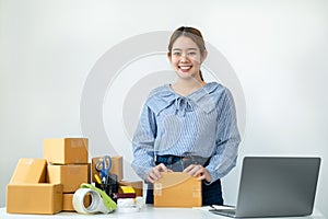 Asian woman small business owner smiling to looking at the camera and standing to holding parcel of box at the table