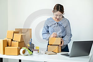 Asian woman small business owner standing to writing customer address on parcel of box and checking information