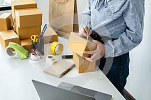 Asian woman small business owner standing to writing customer address on parcel of box and checking information