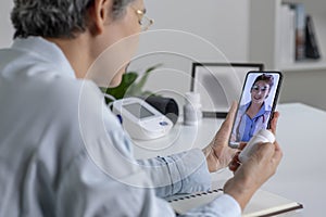 Asian woman with smartphone during an online consultation with her doctor in her living room, telemedicine concept.