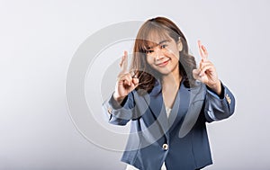 Asian woman smiles confidently in a studio portrait, her fingers crossed as a sign of hope and good