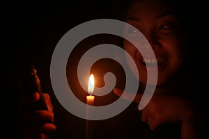 Asian woman smiling to her cellphone with candle in the dark night