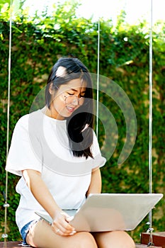 Asian woman smiling while working on her laptop outside the office, at home, working in the park. work holiday at