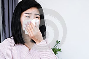 Asian woman sneezing, coughing allergic rhinitis to the bad weather hand holding paper tissue covering her runny nose