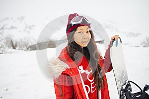 Asian woman in snowboard suit. Sportswoman on a mountain with a snowboard in the hands. Concept on winter sports.