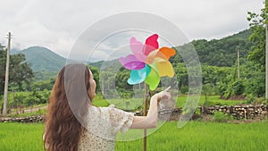 Asian woman spin windmill toy in rice fiend with mountain in background. Nan, Thailand.
