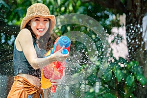 Asian woman splashed by water for Songkran festival. She uses a water gun