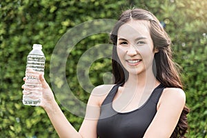 Asian woman in sportswear holding bottle of water on natural background. freshness, happiness, relaxing and smiling.