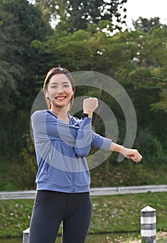 Asian woman in sportswear stretching her arms, warming up before running at the park in the morning