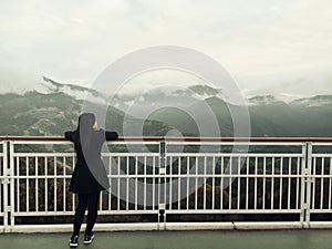 Asian woman standing alone on balcony looking at white foggy and mountains background