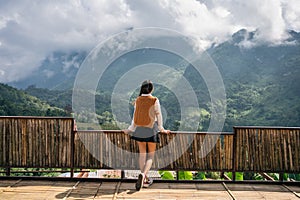 Asian woman standing and enjoying the mountain view on wooden balcony in sunny day
