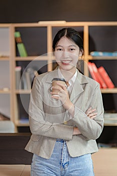 Asian woman standing on front desk while holding coffee cup and looking