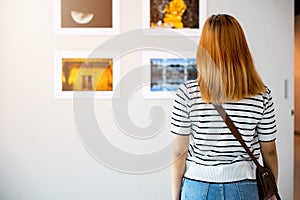 Asian woman standing she looking art gallery in front of colorful framed paintings pictures