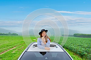 Asian woman standing out of car sunroof. Relaxing and freedom with spring time. Young tourist travel alone in Thailand