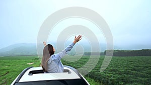 Asian woman standing out of car sunroof. Relaxing and freedom with spring time. Young tourist travel alone in Thailand on summer
