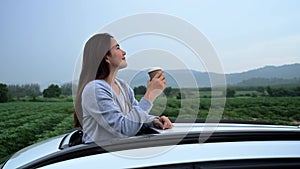 Asian woman standing out of car sunroof. Relaxing and freedom with spring time. Young tourist travel alone in Thailand on summer