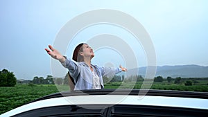 Asian woman standing out of car sunroof. Relaxing and freedom with spring time. Young tourist travel alone in Thailand on summer